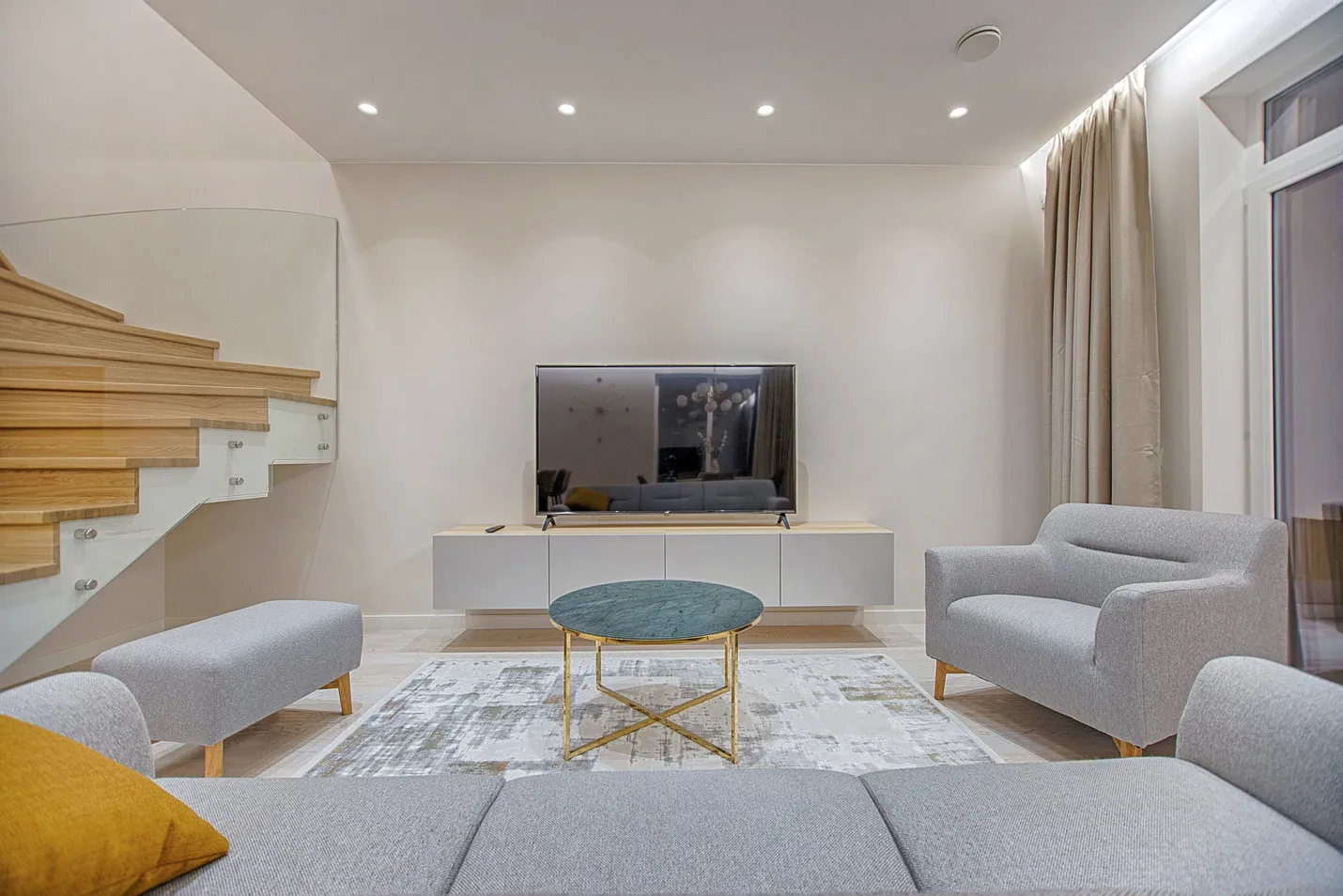 A living room with a grey sofa, a round brass table and a staircase.