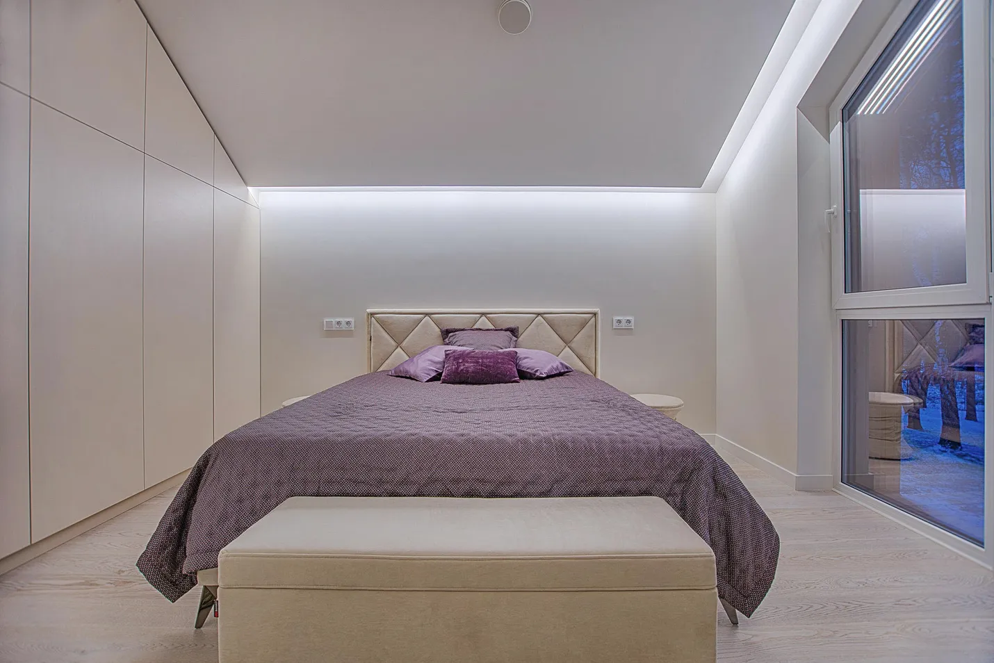 A bedroom with a quilted headboard, a purple bedspread and a bench at its foot.