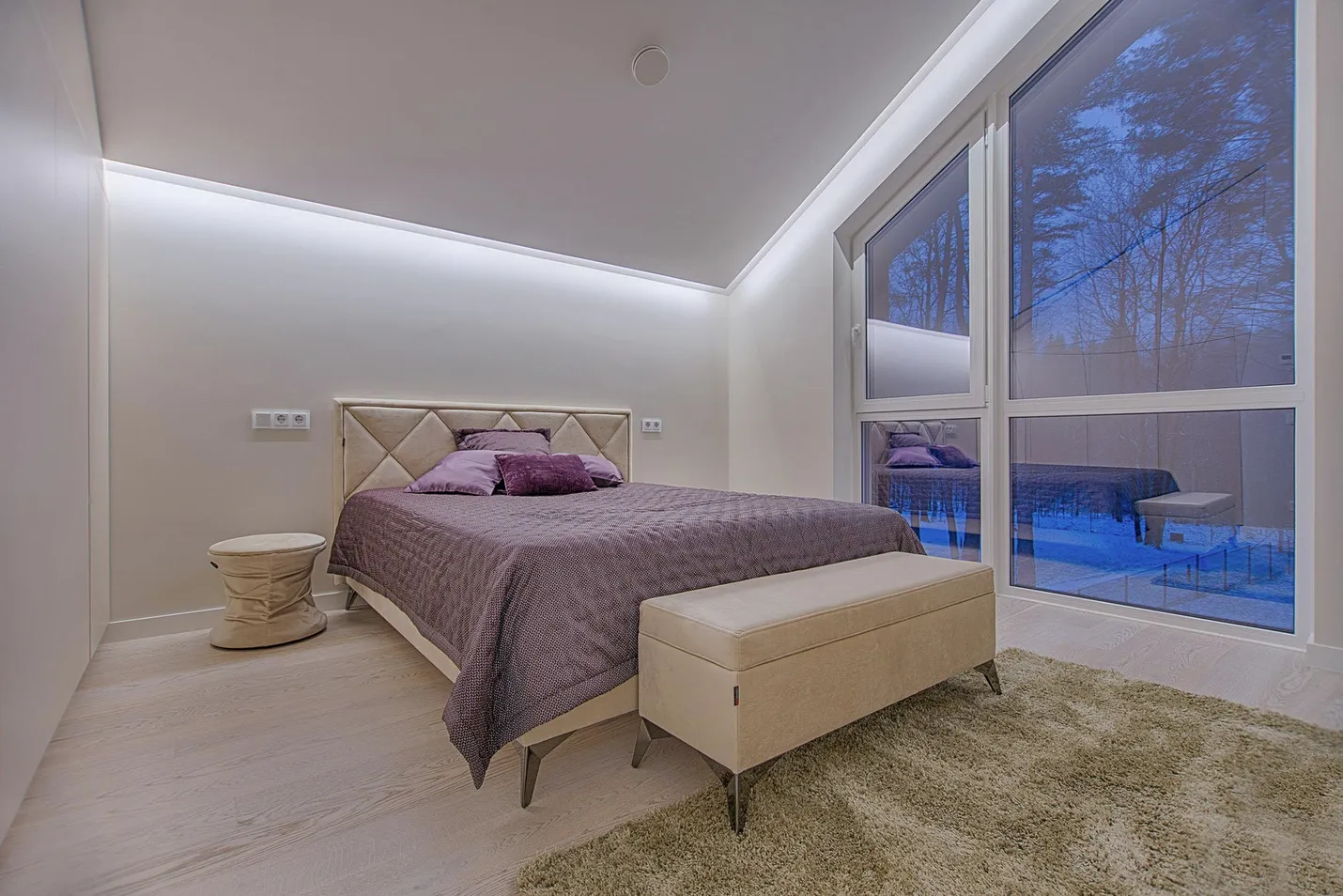 A bedroom with a tall window, a purple bedspread and a deep rug.